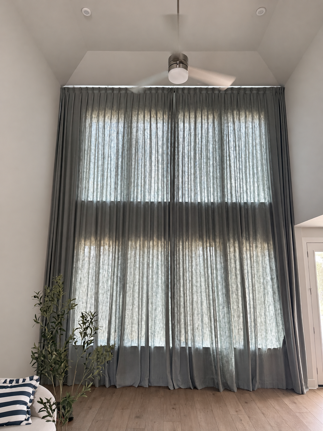 Drawn unlined draperies transmitting daylight over two levels of glazing, with a darker horizontal band over the wall between them.