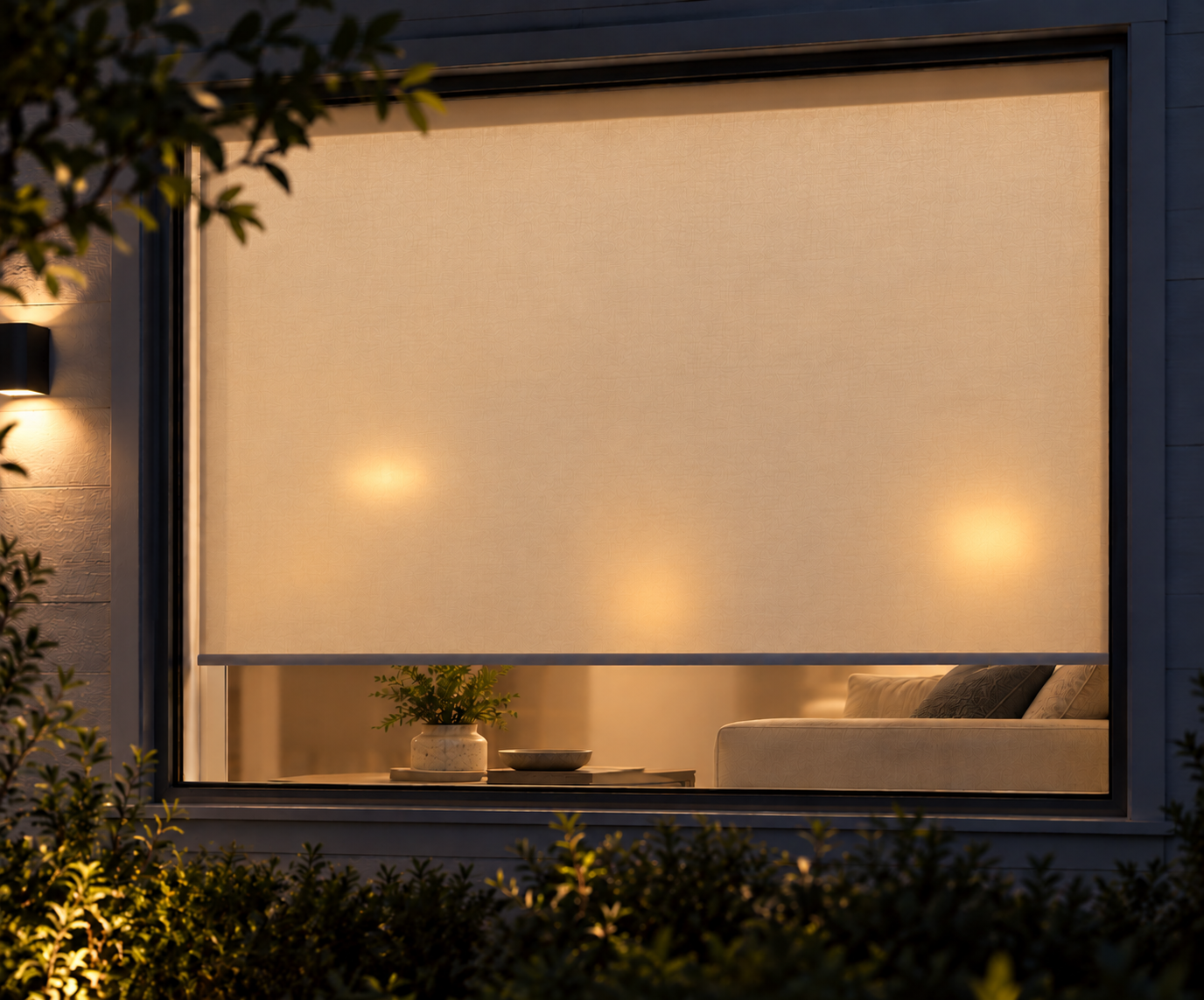 Light-filtering roller shade at night, seen from outside, with indoor light glowing through the fabric