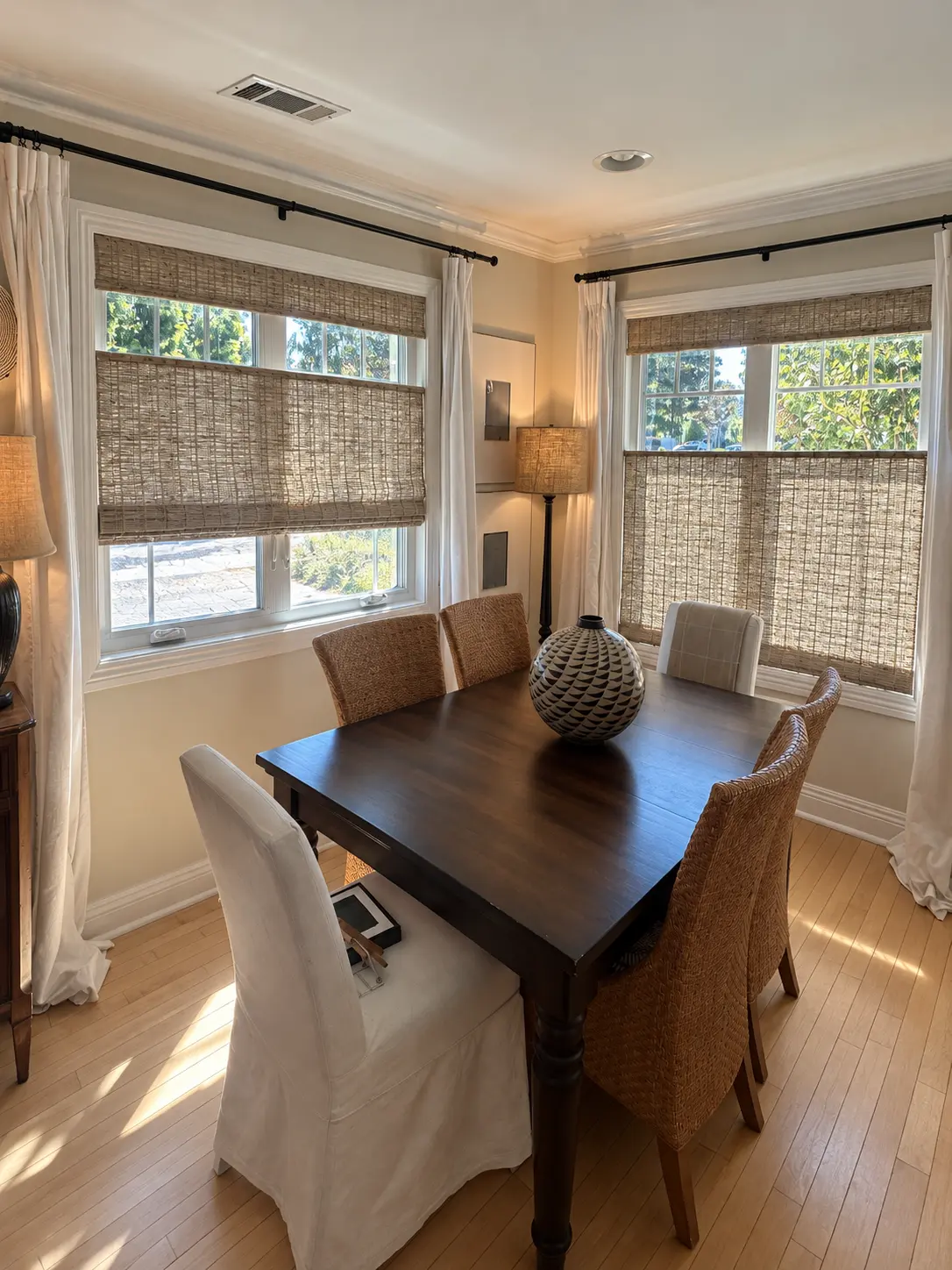 Dining room with Fiji Sandy Fawn shades, a dark wood table, wicker chairs and ivory draperies