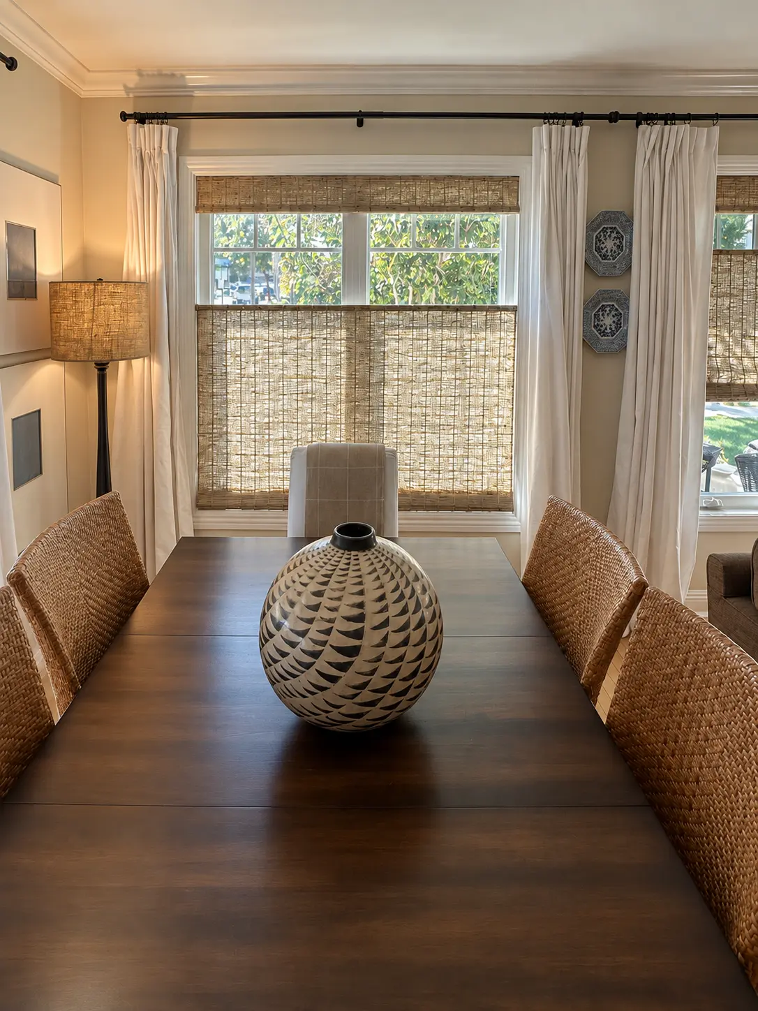 Fiji Sandy Fawn woven shade behind a dining table and patterned ceramic vase